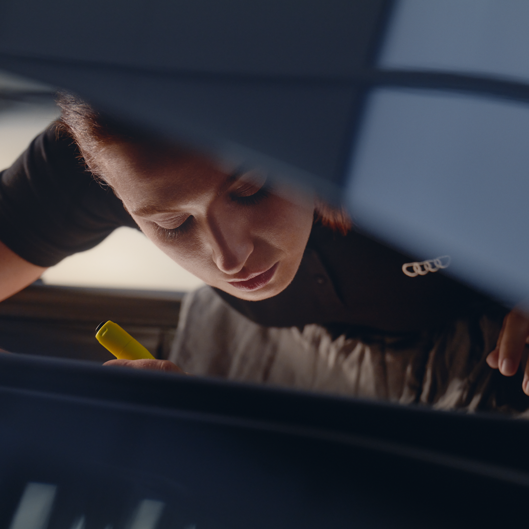 Kvindelig mekaniker, der kigger under motorhjelmen på en Audi